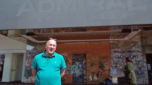 Frank Thannhäuser steht vor dem ehemaligen Eingang der Admiral Spielhalle. Die Fassade ist mit Graffiti und Stickern bedeckt, ein Sperrholzbrett verschließt die Tür. Oben ist der verblasste Schriftzug "Admiral Spielhalle" zu erkennen.