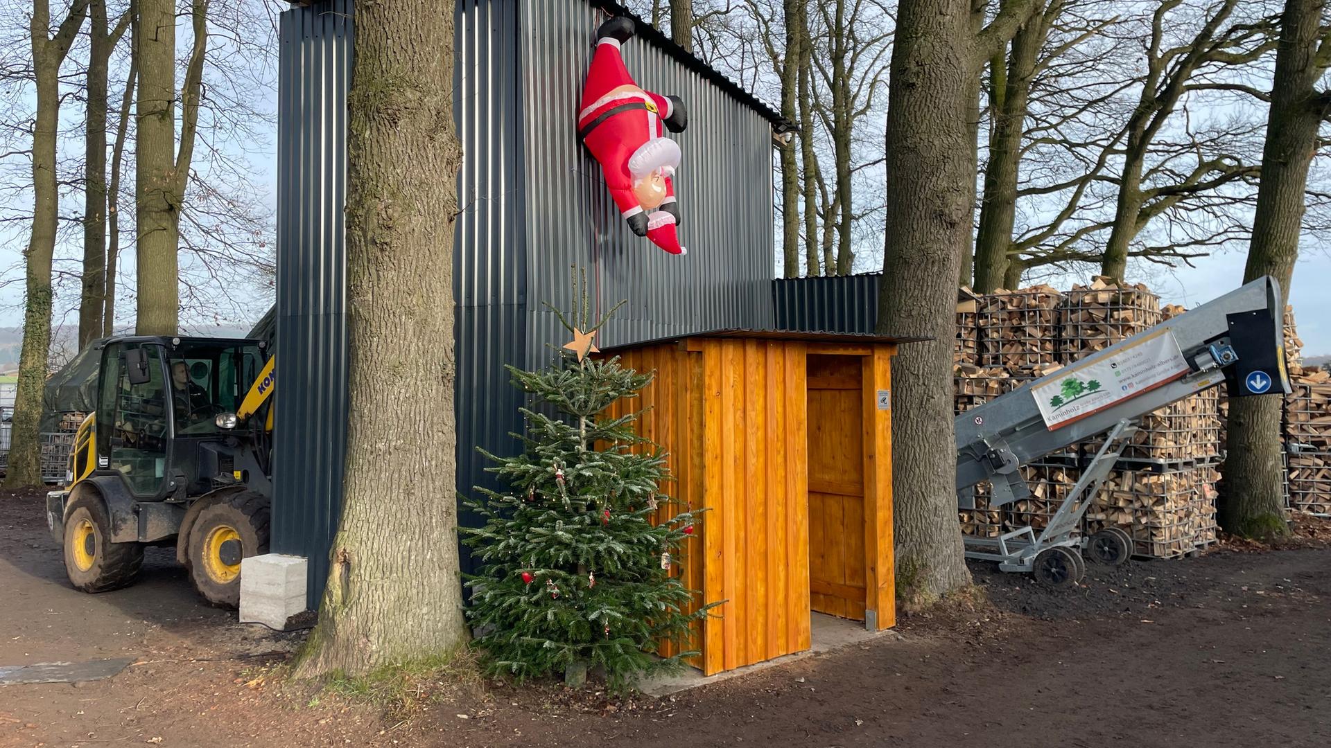 Eine Holzhütte steht zwischen Bäumen, daneben viele Holzscheite in Gitterkäfigen. | NDR, Andreas Gervelmeyer