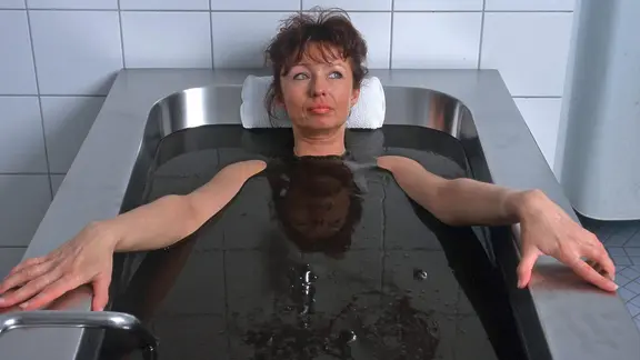 Eine Frau liegt in einer mit Moor gefüllten Badewanne.