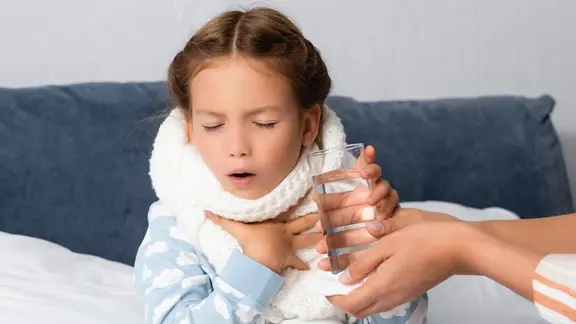 Ein krankes Mädchen sitzt im Bett und hustet.