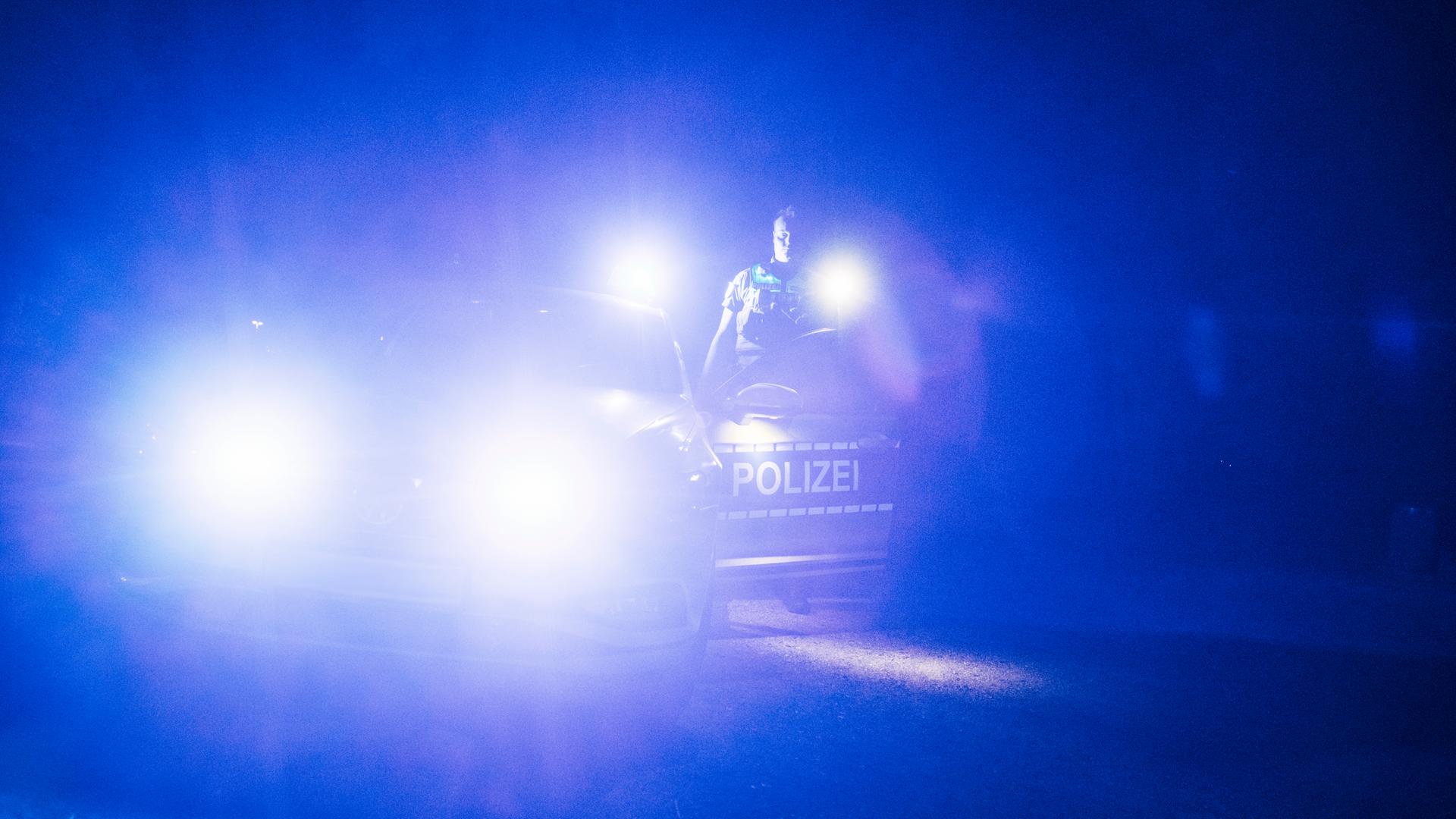 Ein Polizist steht mit einer Taschenlampe neben seinem Dienstfahrzeug. | Julius Matuschik