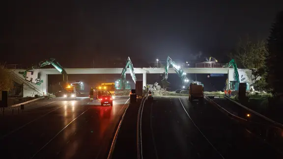 Bagger sind nachts auf der Autobahn A1 unterwegs, um eine Brücke abzureißen.