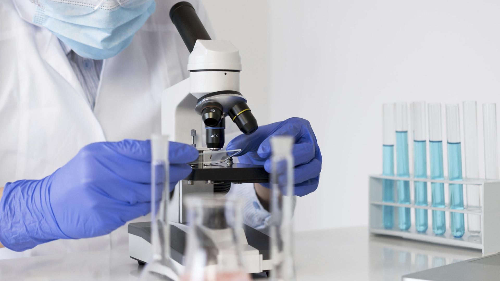 Eine Frau in Schutzkleidung hält eine Probe unter ein Gerät im Labor. | picture alliance/imageBROKER, Oleksandr Latkun