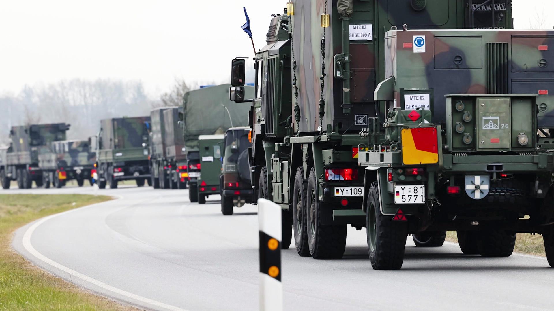 Eine Kolonne von Militärfahrzeugen fährt auf einer kurvigen Landstraße, alle Fahrzeuge sind in Tarnfarben lackiert und eng hintereinander gereiht. | Screenshot