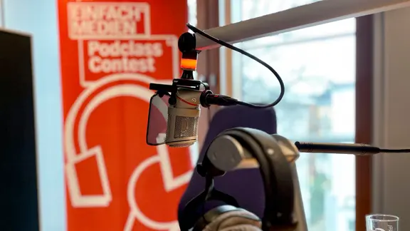 Ein Mikrofon und Kopfhörer. Dahinter ein Banner vom NDR einfach.Medien Podclass Contest.