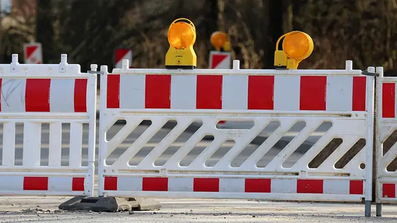 Eine Straße ist mit Warnbaken und einem Zaun abgesperrt.