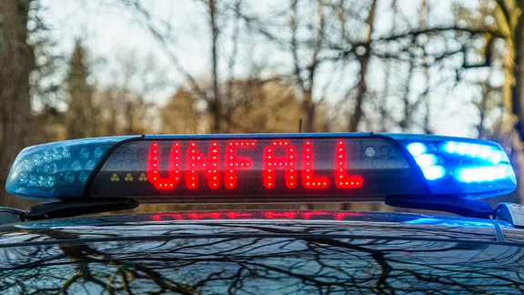 Auf einer Strasse steht ein Einsatzfahrzeug der Polizei mit Blaulicht und dem Schriftzug Unfall bei einem Verkehrsunfall.