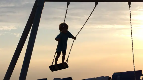 Ein Kind schaukelt im Sonnenuntergang.