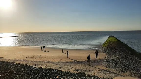Bei einem Strandspaziergang kann man Ebbe und Flut intensiv erleben. | NDR, Christina Maciejewski Menschen stehen im Sonnenuntergang am Nordseestrand der Insel Baltrum