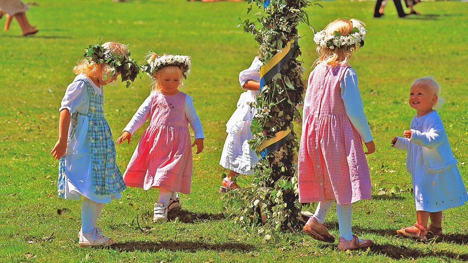 Traditionell schmücken sich vor allem Kinder zum Mittsommerfest mit Blumenkränzen. | picture-alliance / HB- Verlag, Michael Riehle Kinder mit Blumenkränzen tanzen in Schweden um eine geschmückte Stange zum Mittsommerfest.