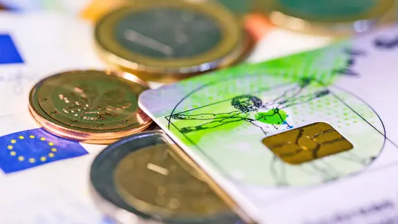 Eine Krankenkassenkarte und Münzen liegen auf einem Tisch.