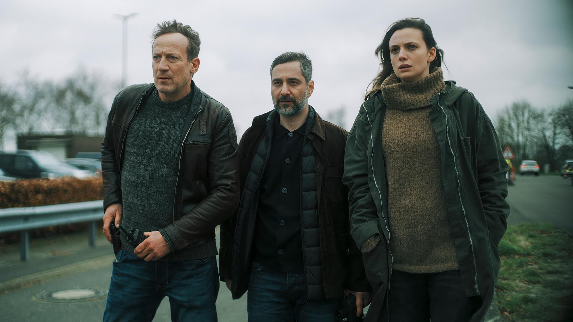 Zwei Männer und eine Frau laufen auf einem Parkplatz. | NDR/Georges Pauly