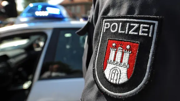Ein Beamter der Polizei Hamburg vor einem Streifenwagen. | dpa - Bildfunk, Marcus Brandt Ein Beamter der Polizei Hamburg vor einem Streifenwagen.