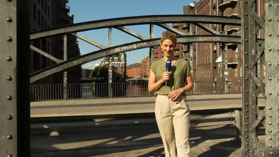 Moderatorin Eva Diederich steht mit Mikrophon auf der Poggenmühlen-Brücke in der Hamburger Speicherstadt.