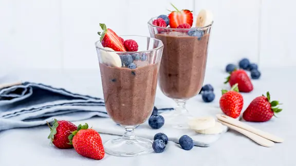 Zwei Gläser mit Schoko-Eiscreme, garniert mit Beeren, stehen auf einem Tisch.
