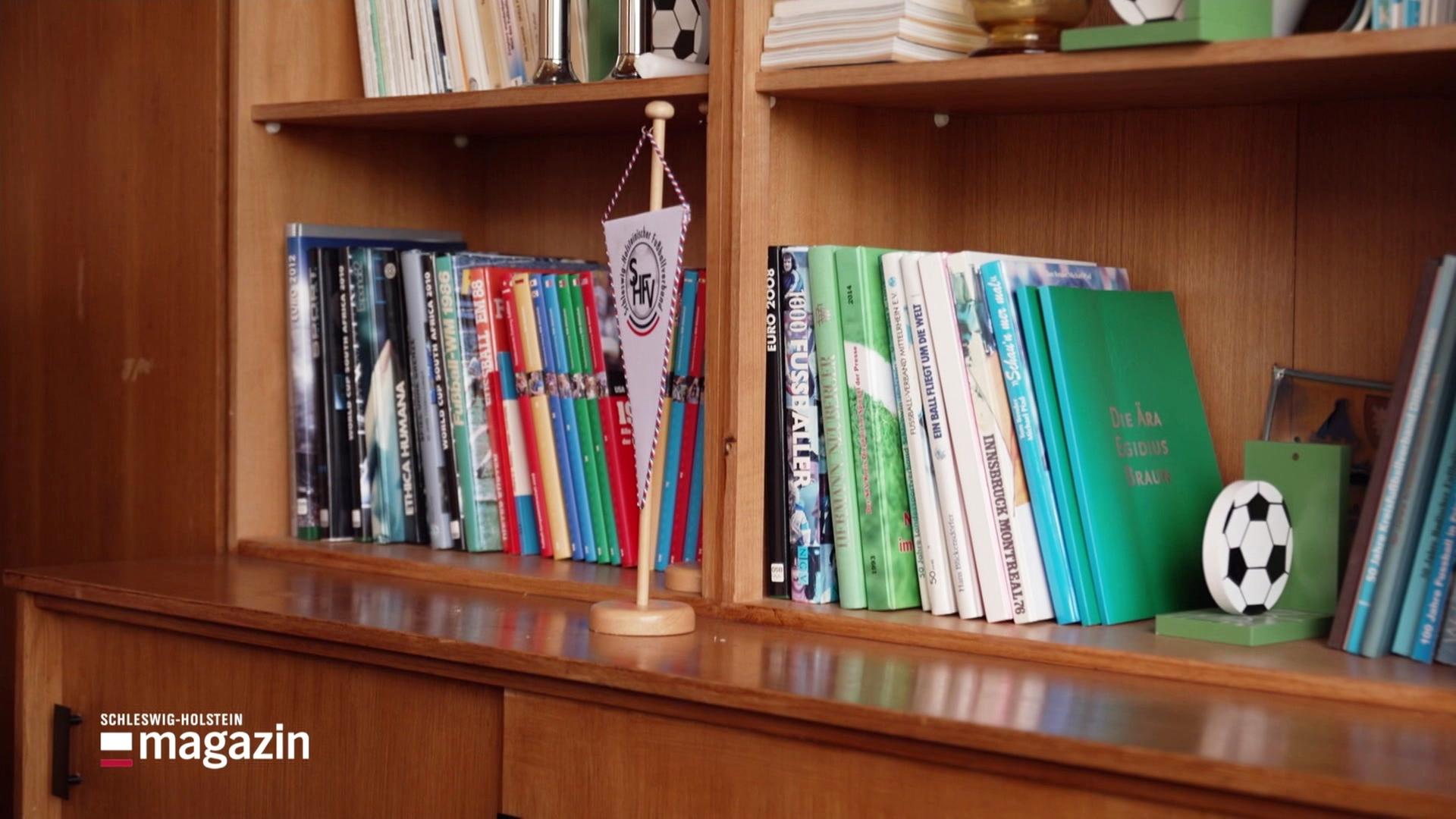 Ein Fußballwimpel steht auf einem Holzschrank. | Screenshot