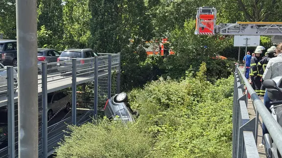 Am Parkhaus des AK barmbek in Hamburg ist ein Auto in einen Grünzu gestürzt. Einsatzkräfte der Feuerwehr sind rechts zu sehen. 