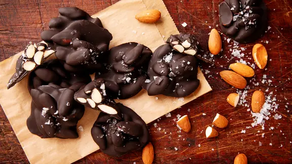 Auf einem Holzbrett liegen mit Schokolade überzogene Mandeln, darauf etwas Meersalz. | NDR, Claudia Timmann Auf einem Holzbrett liegen mit Schokolade überzogene Mandeln, darauf etwas Meersalz.