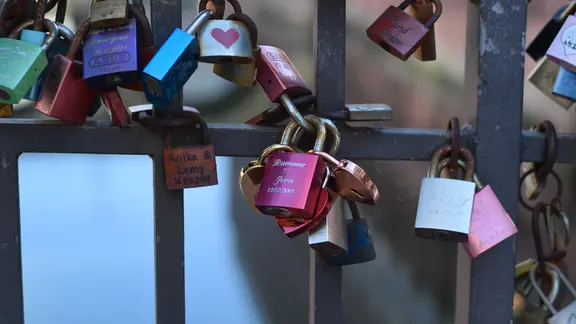 Liebesschlösser mit eingravierten Namen hängen an einer Brücke.