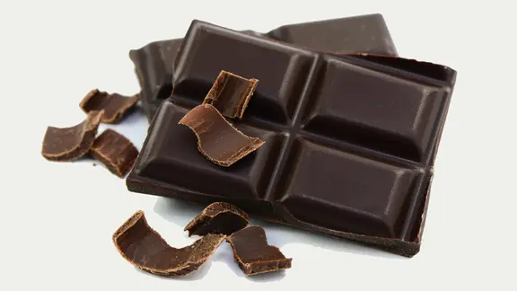 Dunkle Schokolade enthält weniger Zucker und Kalorien als helle. | Fotolia, photocrew Mehrere Stücke und einige Späne dunkle Schokolade.