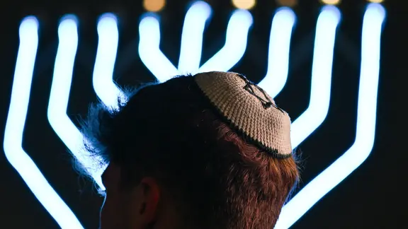 Un homme porte un kippa, en arrière-plan, un lustre de Chanukka brille. | DPA - Alliance Picture, Arne Deder Un homme porte un kippa, en arrière-plan, un lustre de Chanukka brille.
