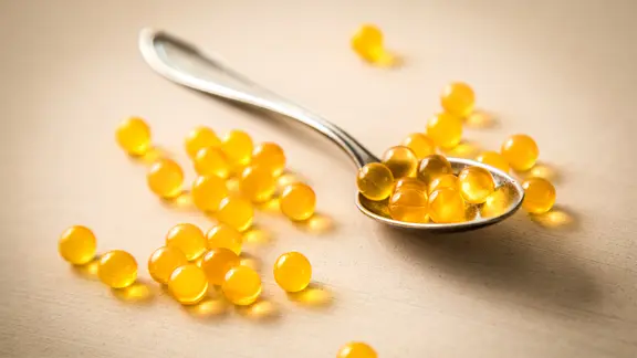 Mehrere Vitamin-D-Tabletten auf einem Löffel, andere liegen drum herum verstreut auf dem Tisch.