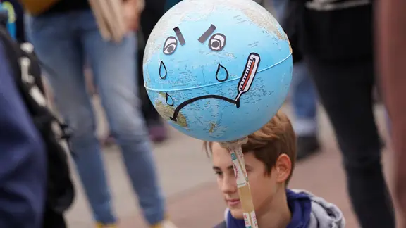 Bei einer Klimastreik-Demo in Hamburg hält ein Junge eine Erdkugel, die weint.