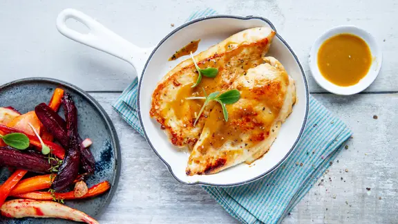 Hähnchenbrust in einem kleinen Topf, ein Teller mit Ofengemüse und ein Schälchen mit Marinade stehen auf dem Tisch.
