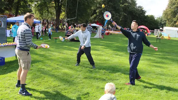 Menschen spielen auf einer Wiese mit Tennisschlägern.