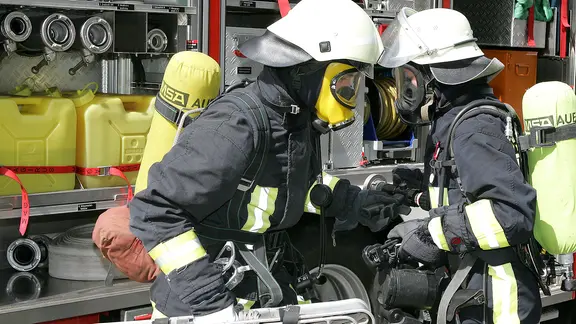 Zwei Feuerwehrleute an einem Einsatzfahrzeug.
