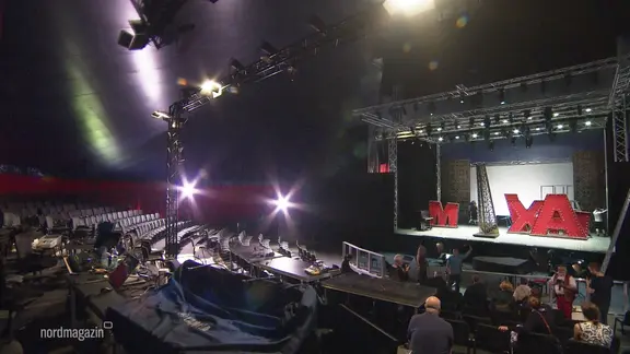 In einem größeren Zelt sind eine Theaterbühne und eine größere Zuschauertribüne aufgebaut.