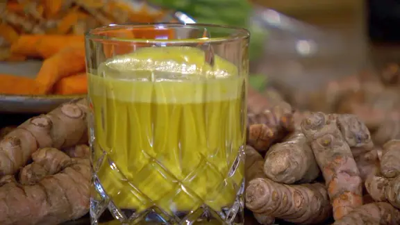 Ein Glas mit Goldener Milch steht vor Kurkuma-Wurzeln. | NDR, Screenshot NDR Ein Glas mit Goldener Milch steht vor Kurkuma-Wurzeln.