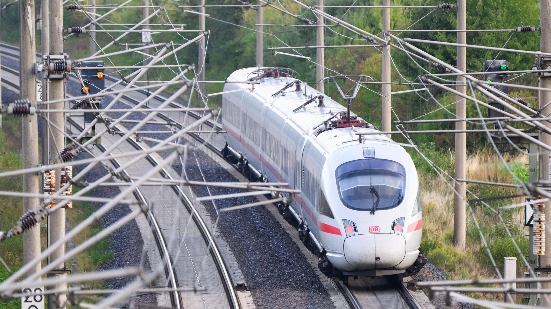 Ein ICE der Deutschen Bahn fährt, mehrere Oberleitungen im Vordergrund. | picture alliance/dpa
