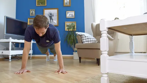 Jonas W. trainiert täglich zu Hause. | NDR, Oliver Zydek Junger Mann macht im Wohnzimmer Liegestütz.