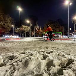 Eine Frau fährt am Abend mit einem Fahrrad durch das verschneite Hannover.