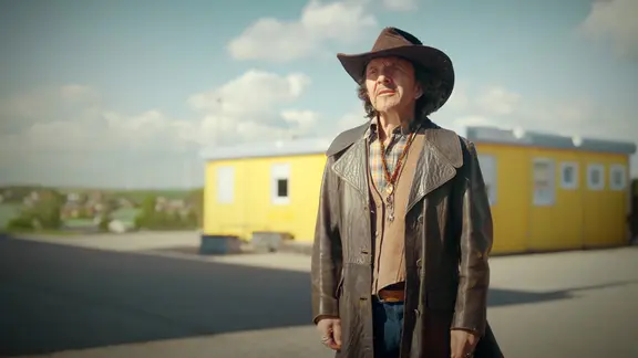 Mann mit Cowboyhut steht vor gelbem Container
