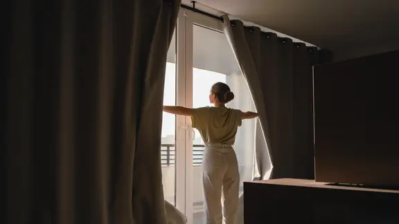 Frau öffnet die Vorhänge eines Hotelzimmers