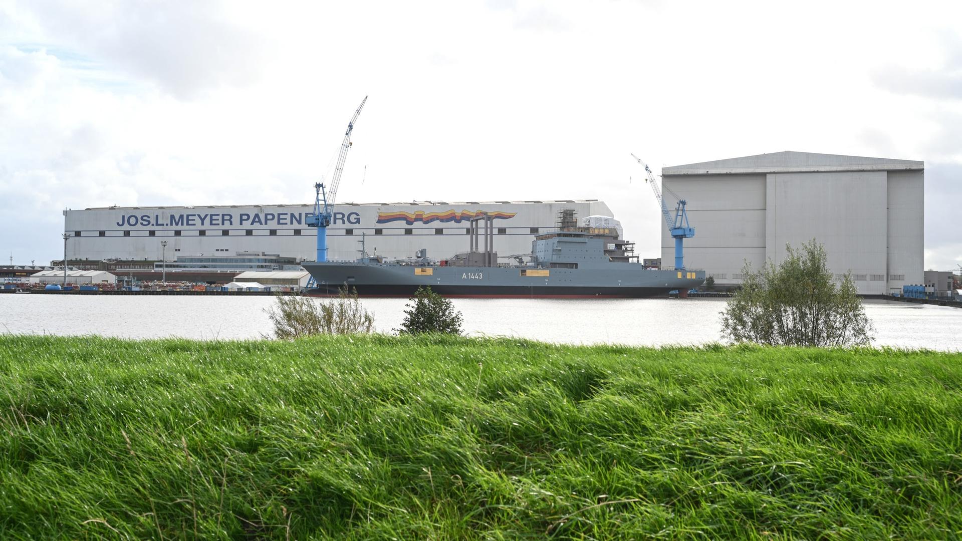 Ein Schiff liegt vor der Meyer Werft, Blick von der anderen Uferseite. | picture alliance/dpa, Lars Penning