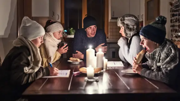 Fünf Personen sitzen in Winterkleidung an einem mit Kerzen beleuchteten Tisch. 