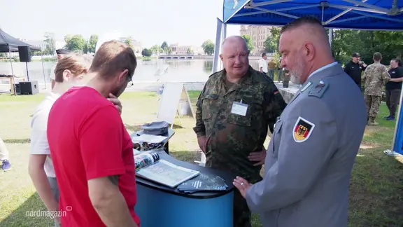 Zwei Männer informieren sich an einem Stand an dem zwei Bundeswehrsoldaten stehen.