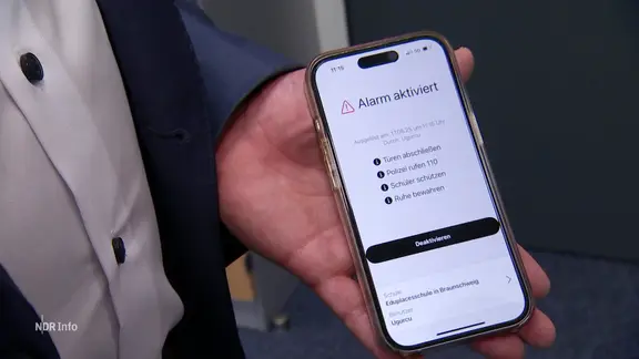 Ein Mann hält ein Smartphone mit einem Alarmsystem in der Hand.