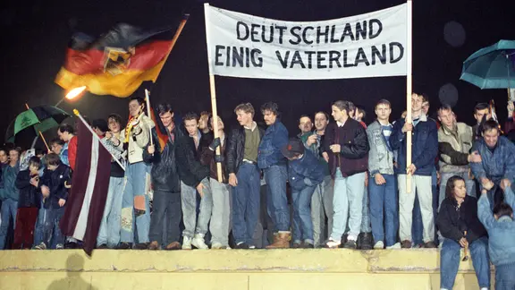 Mit der Deutschlandfahne und einem Transparent "Deutschland Einig Vaterland" stehen zahlreiche Berliner am 22. Dezember 1989 auf der Berliner Mauer am Brandenburger Tor.
