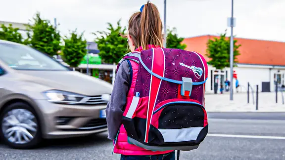Eine Schülerin mit Schulranzen vor einer Straße mit Autos. (extra 3 vom 04.04.2024 im Ersten)