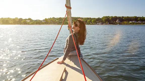 Einer Frau sitzt vorne auf einem Boot und lacht in die Kamera.