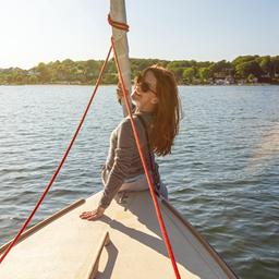 Einer Frau sitzt vorne auf einem Boot und lacht in die Kamera.