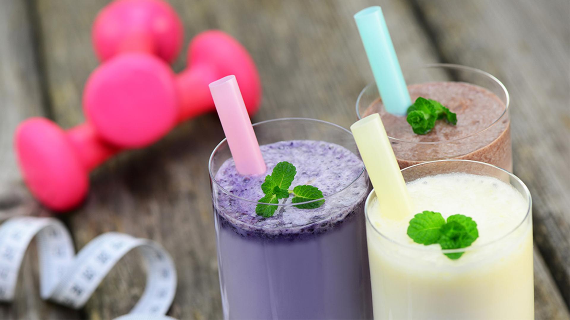 Drei Eiweißshakes auf einem Holztisch, daneben eine Hantel und ein Maßband. | fotolia.com, Printemps
