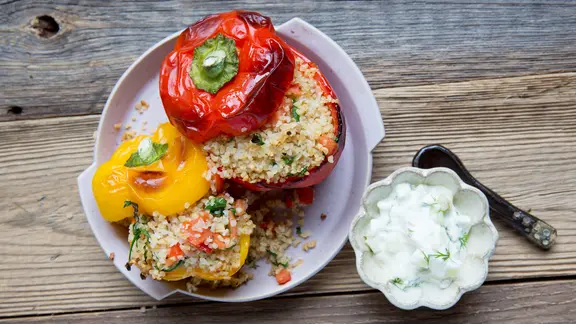 Ein Teller mit zwei gefüllten Bulgurpaprikas und ein Schälchen mit Gurkenquark stehen auf dem Tisch.