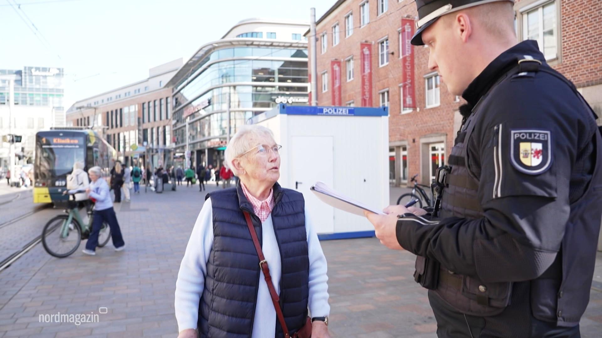 Eine Seniorin wird auf der Straße von einem Polizeibeamten befragt. | Screenshot