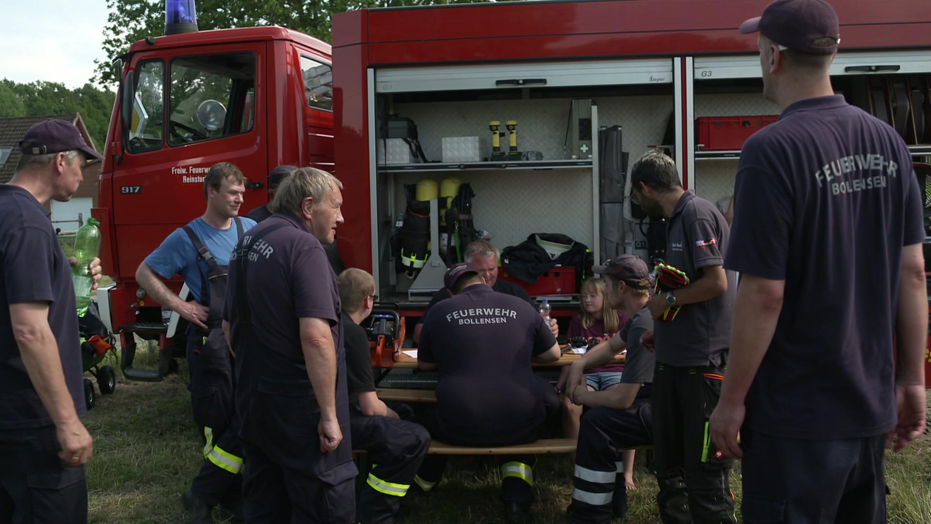 Die Truppe der freiwilligen Feuerwehr Bollensen sitzt gemeinsam an einem Einsatzwagen. | NDR