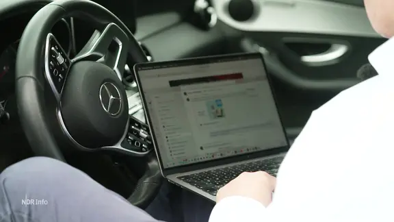 Ein Mann arbeitet im Auto an seinem Laptop.